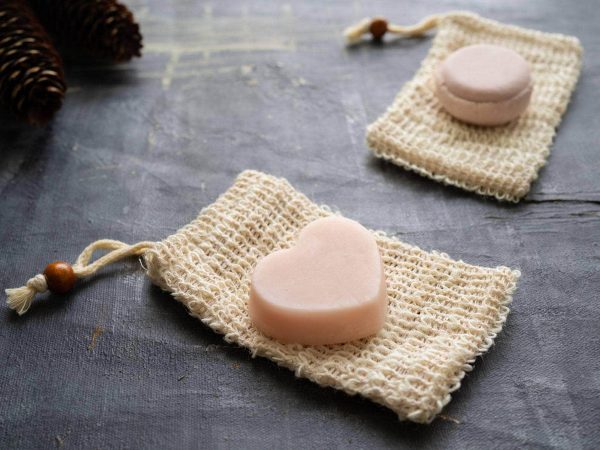 Plantish Future Beauty and Bathroom Pink Heart-shaped Nourishing Conditioner Bar laying on top of a white drawstring soap saver bag.